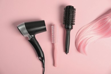 Photo of Stylish round brushes, hairdryer and lock of dyed hair on pink background, flat lay