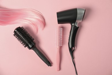 Photo of Stylish round brushes, hairdryer and lock of dyed hair on pink background, flat lay