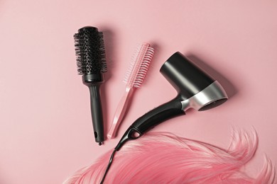 Photo of Stylish round brushes, hairdryer and lock of dyed hair on pink background, flat lay