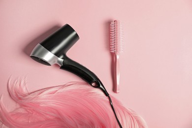 Photo of Stylish round brush, hairdryer and lock of dyed hair on pink background, flat lay. Space for text