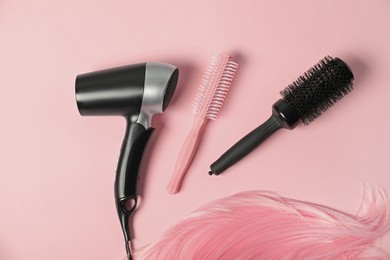 Photo of Stylish round brushes, hairdryer and lock of dyed hair on pink background, flat lay