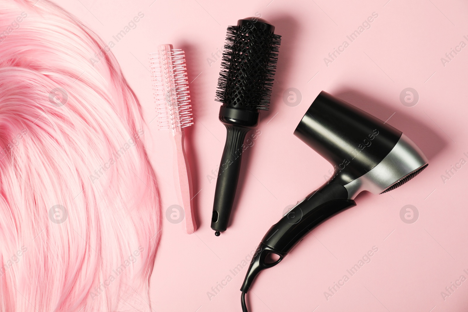 Photo of Stylish round brushes, hairdryer and lock of dyed hair on pink background, flat lay