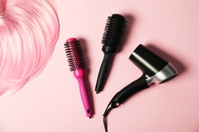 Photo of Stylish round brushes, hairdryer and lock of dyed hair on pink background, flat lay