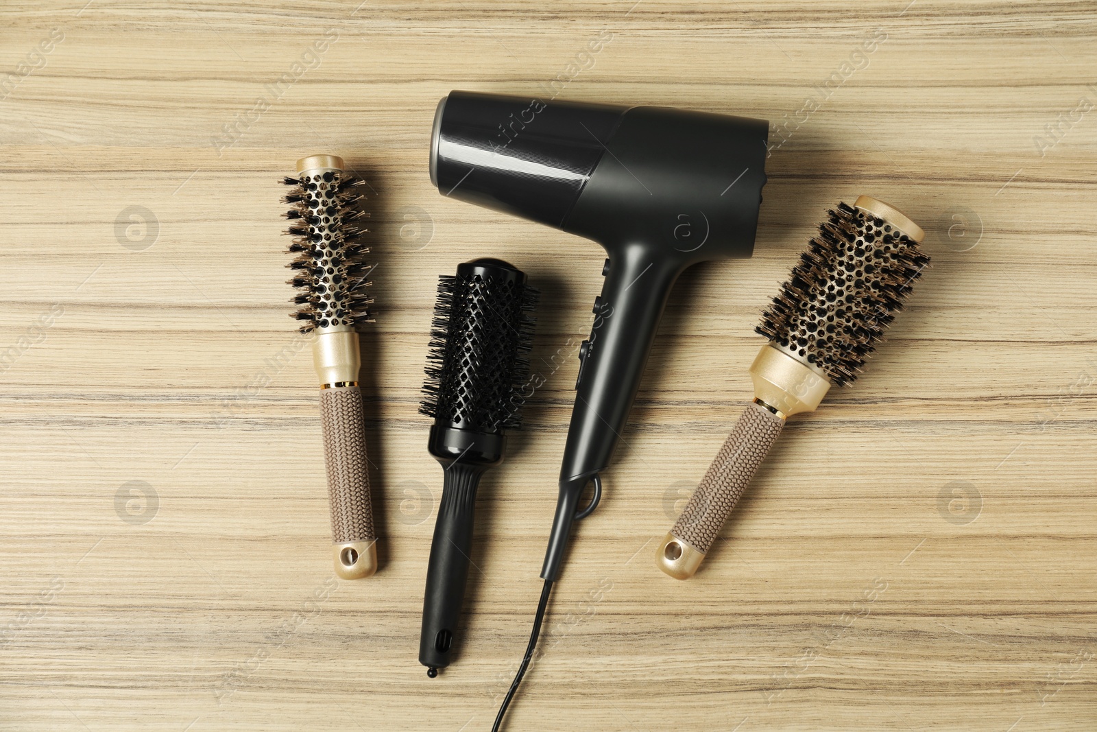 Photo of Stylish round brushes and hairdryer on wooden table, flat lay