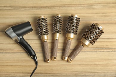 Photo of Stylish round brushes and hairdryer on wooden table, flat lay