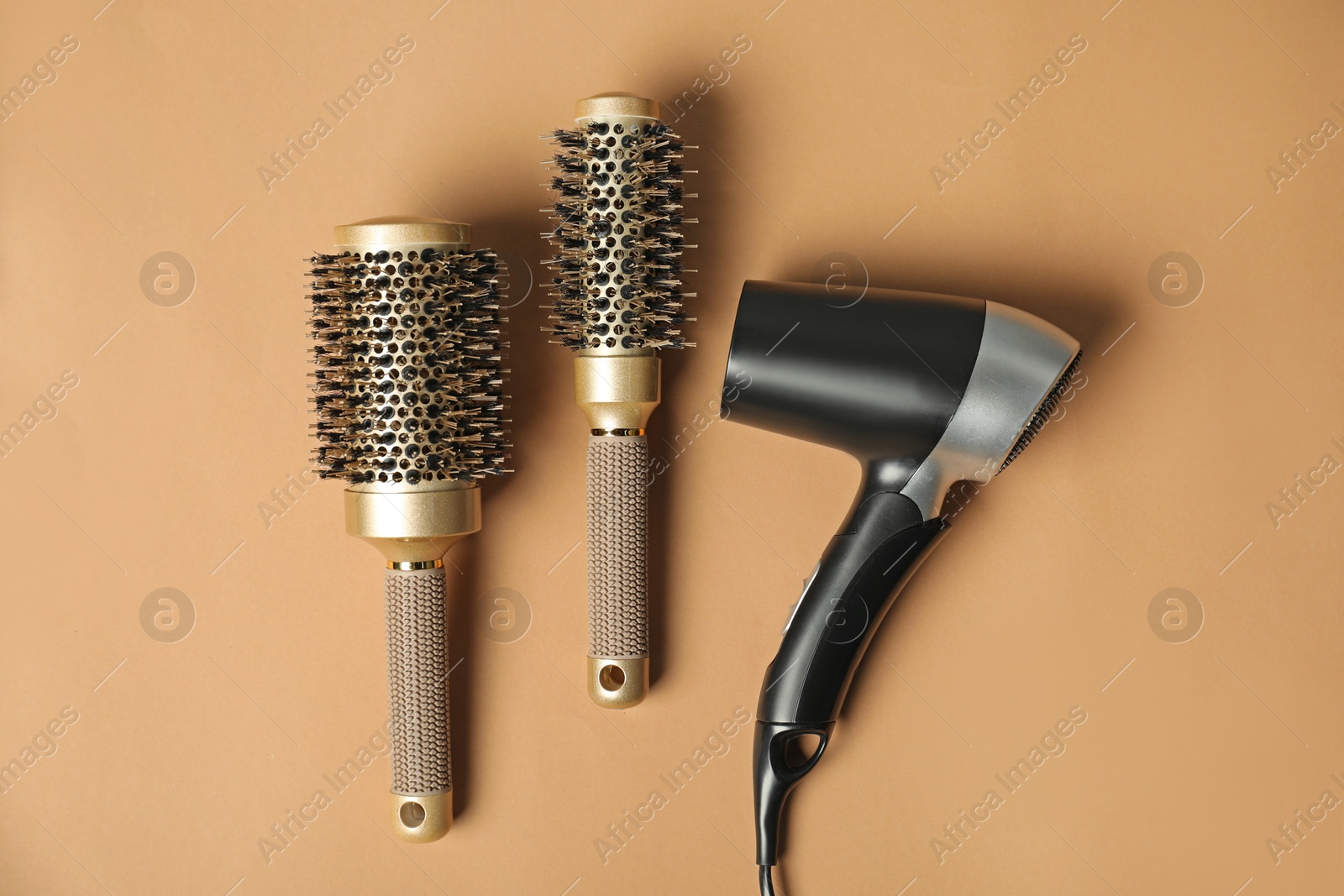 Photo of Stylish round brushes and hairdryer on light brown background, flat lay