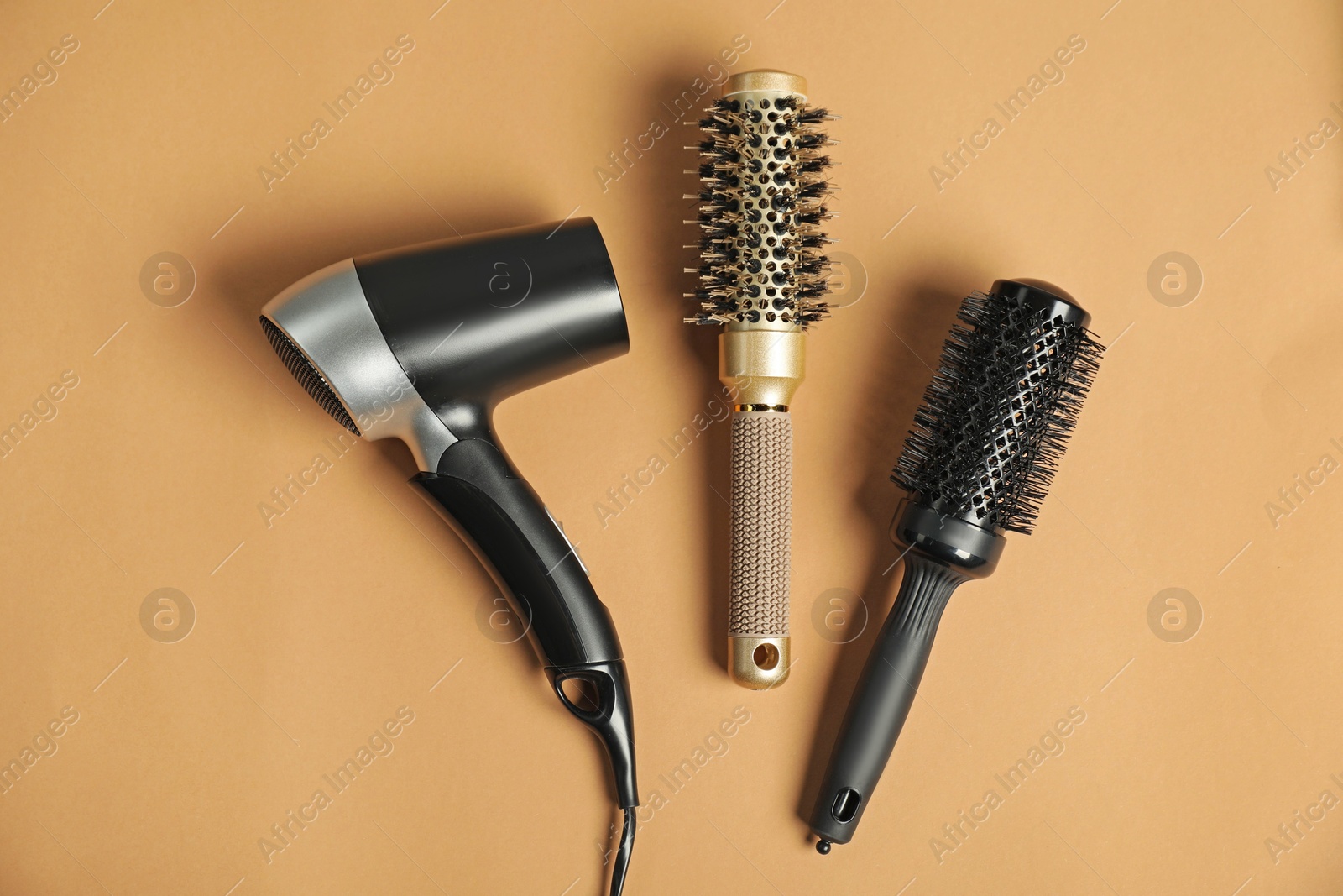 Photo of Stylish round brushes and hairdryer on light brown background, flat lay