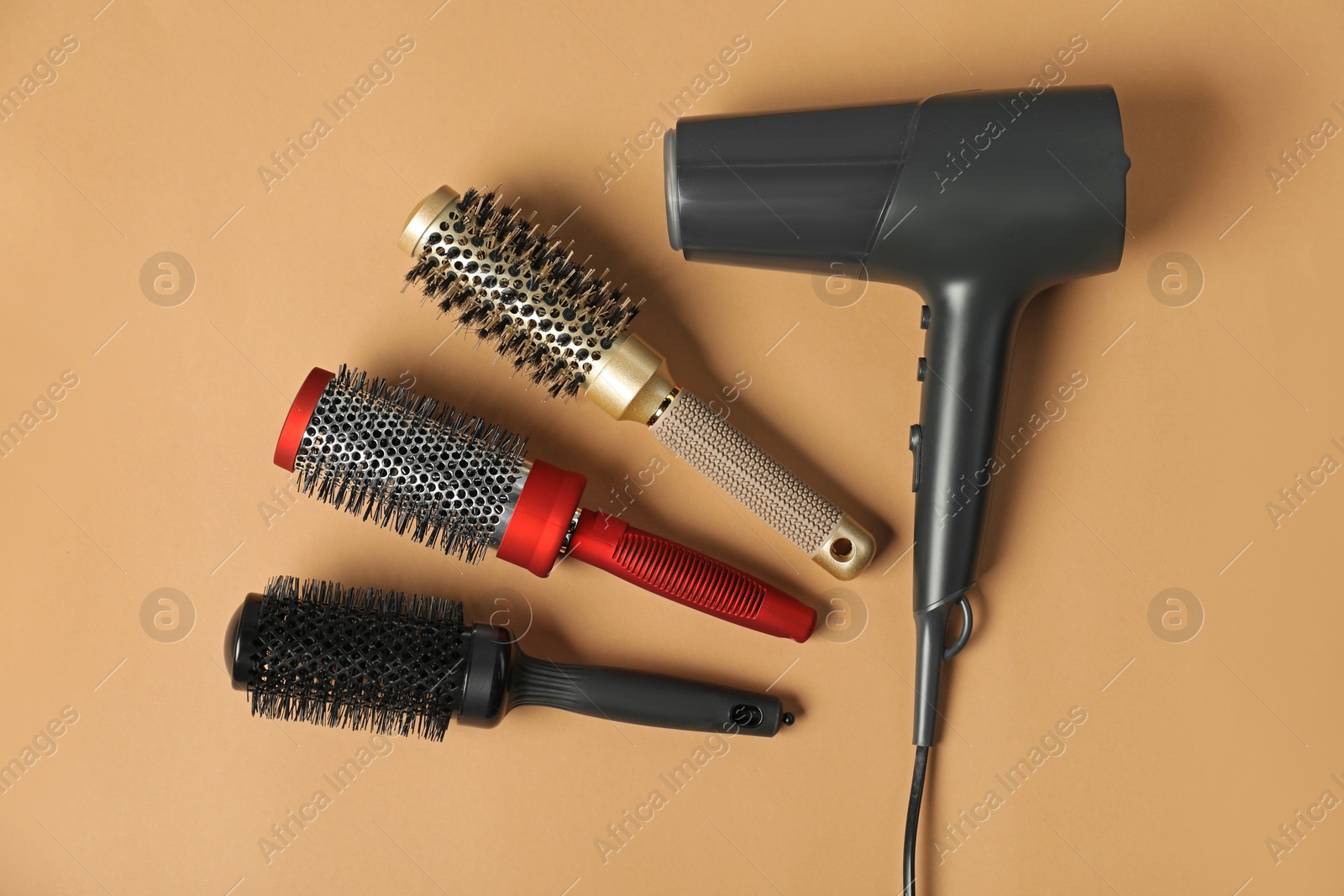 Photo of Stylish round brushes and hairdryer on light brown background, flat lay