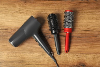 Photo of Stylish round brushes and hairdryer on wooden table, flat lay