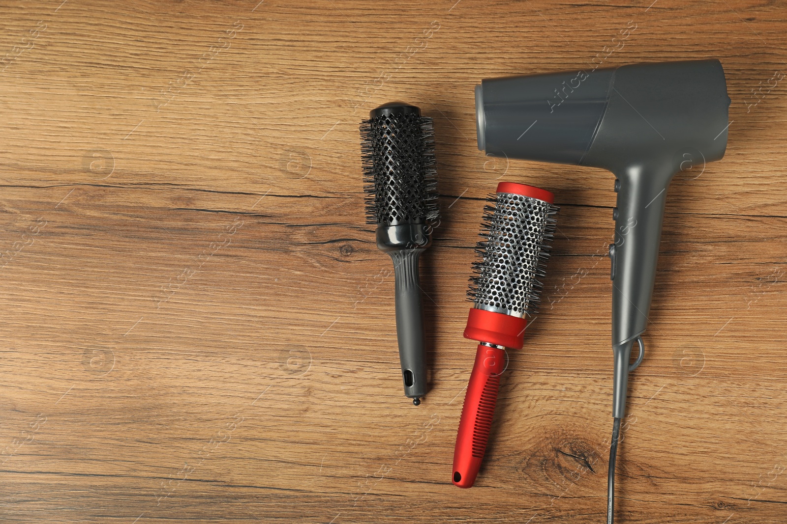 Photo of Stylish round brushes and hairdryer on wooden table, flat lay. Space for text