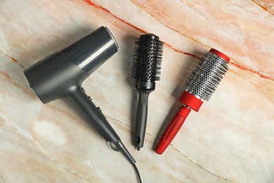 Photo of Stylish round brushes and hairdryer on pink marble table, flat lay