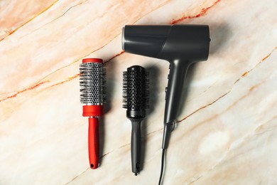 Photo of Stylish round brushes and hairdryer on pink marble table, flat lay