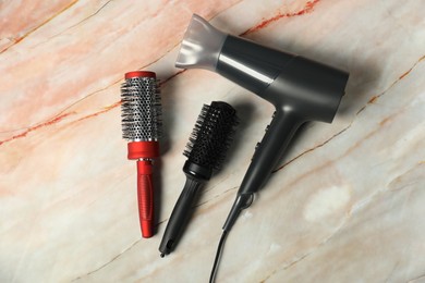 Photo of Stylish round brushes and hairdryer on pink marble table, flat lay