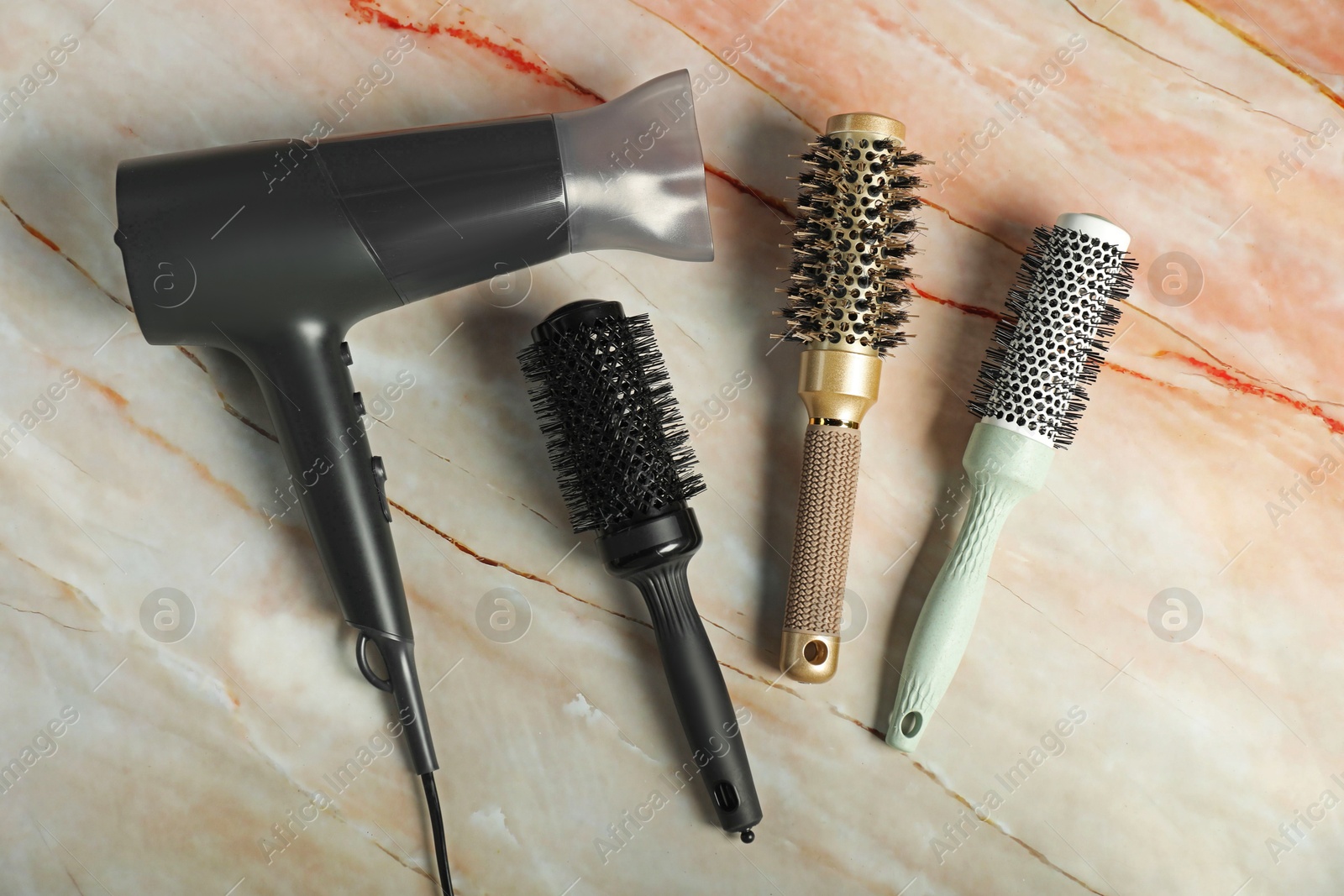 Photo of Stylish round brushes and hairdryer on pink marble table, flat lay