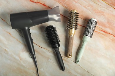 Photo of Stylish round brushes and hairdryer on pink marble table, flat lay