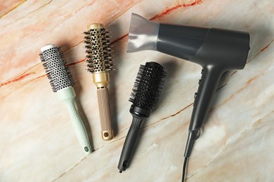 Photo of Stylish round brushes and hairdryer on pink marble table, flat lay