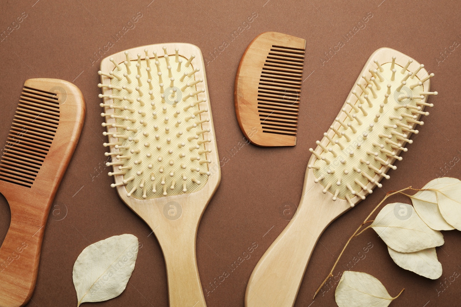 Photo of Wooden hair brushes, combs and leaves on brown background, flat lay