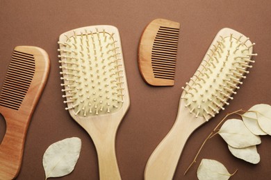 Photo of Wooden hair brushes, combs and leaves on brown background, flat lay