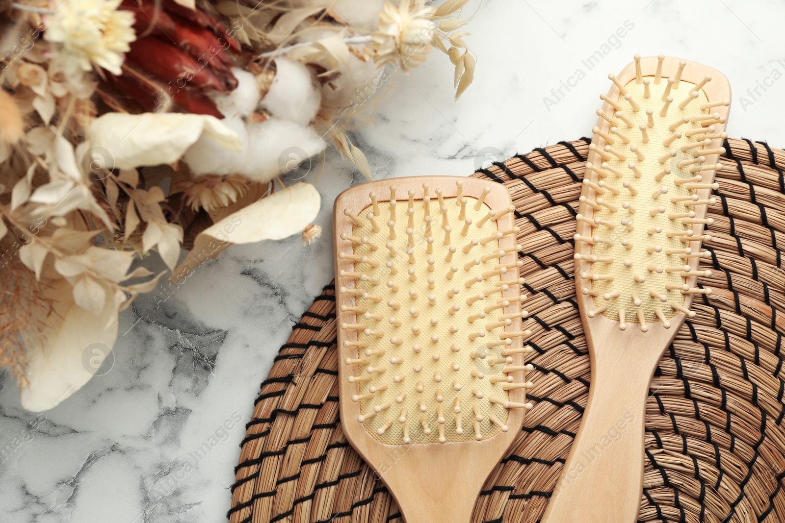 Photo of Wooden hair brushes and dried flowers on white marble background, flat lay