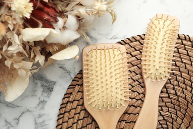 Photo of Wooden hair brushes and dried flowers on white marble background, flat lay