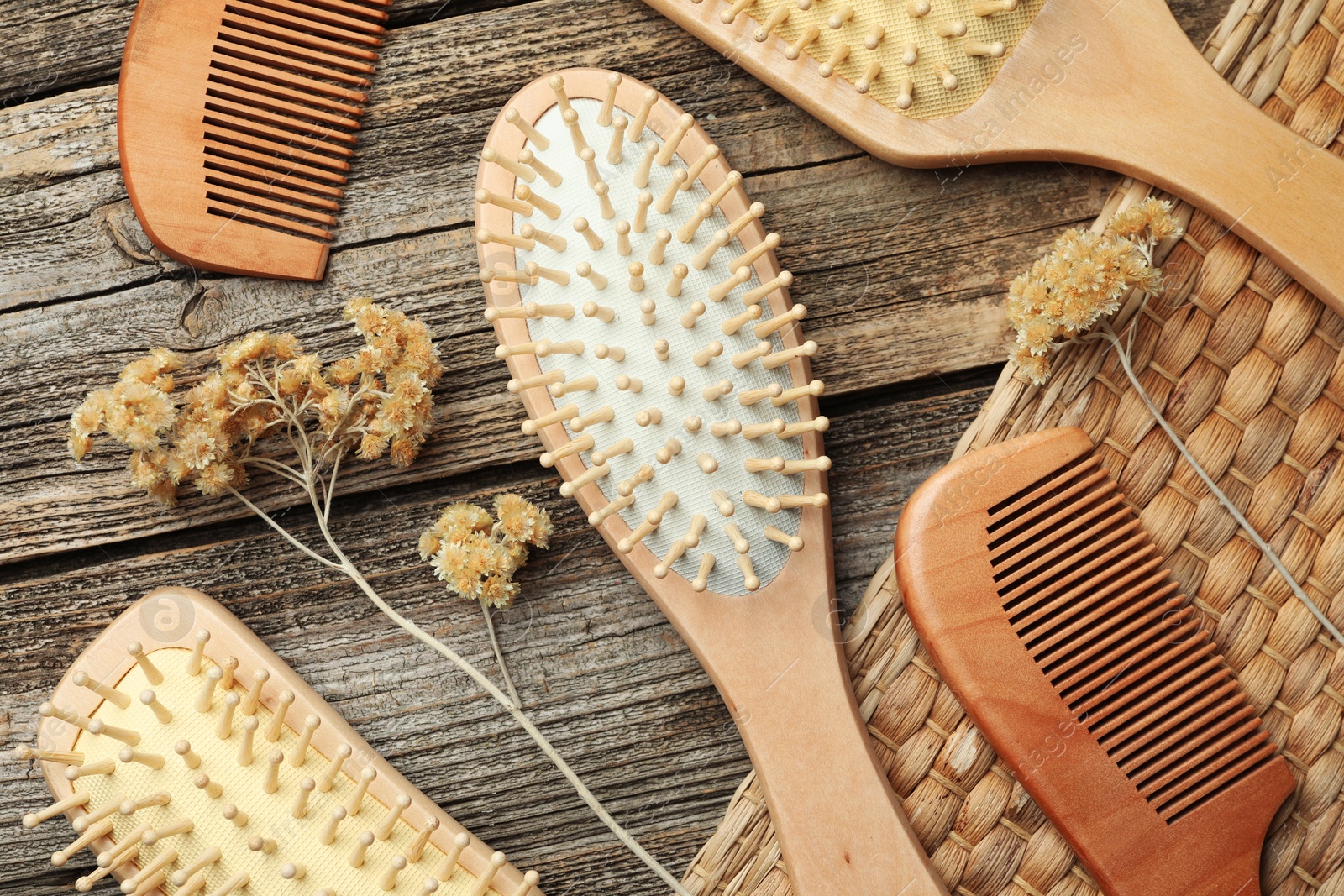 Photo of Hair brushes, combs and dried flowers on wooden background, flat lay