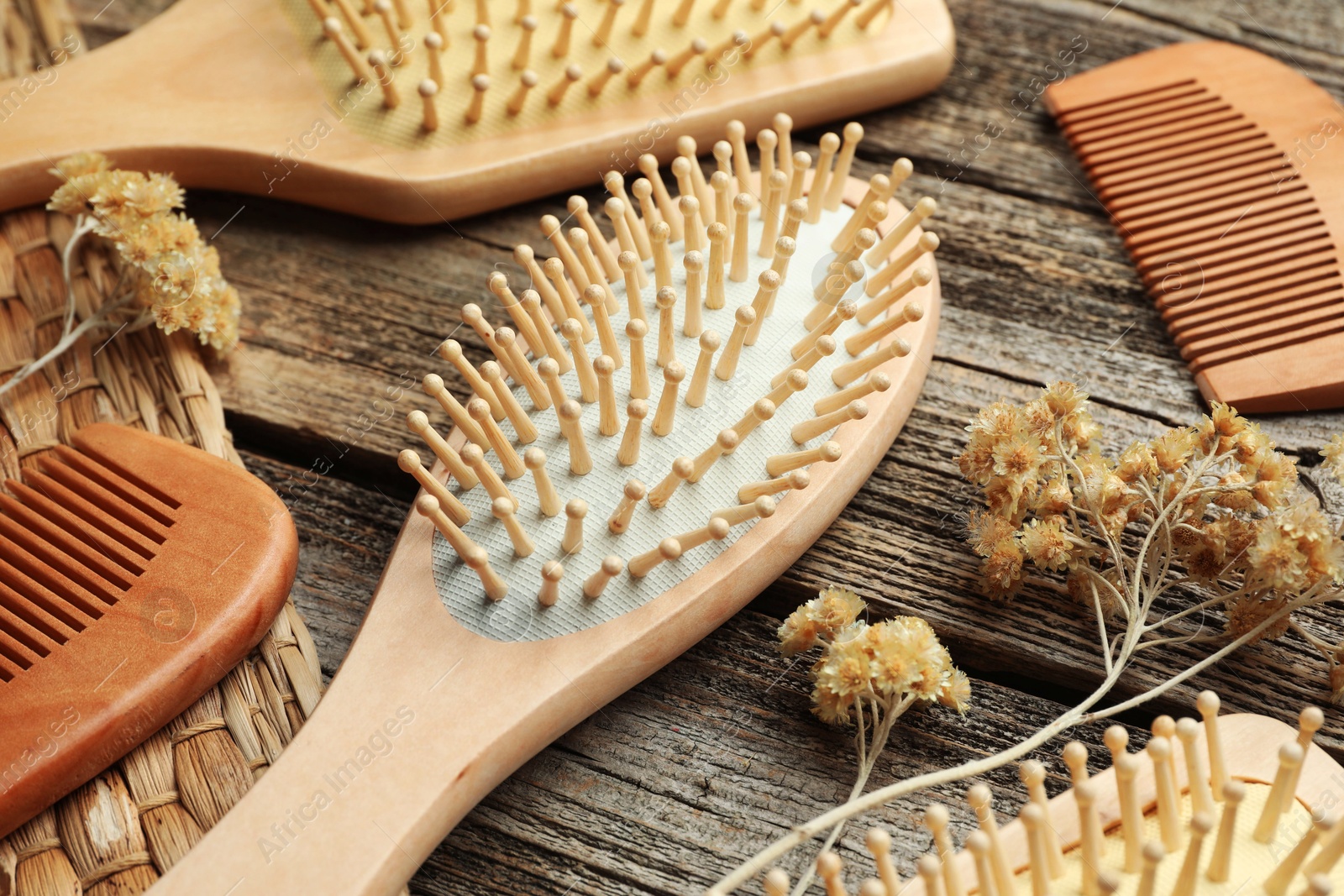 Photo of Hair brushes, combs and dried flowers on wooden background, closeup