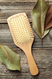 Photo of Hair brush and leaves on wooden background, top view