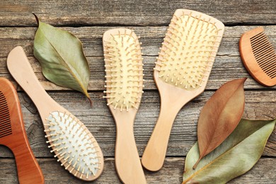 Photo of Hair brushes, combs and leaves on wooden background, flat lay