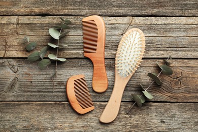 Photo of Hair brush, combs and eucalyptus on wooden background, flat lay