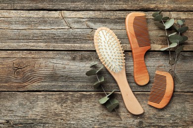 Photo of Hair brush, combs and eucalyptus on wooden background, flat lay. Space for text