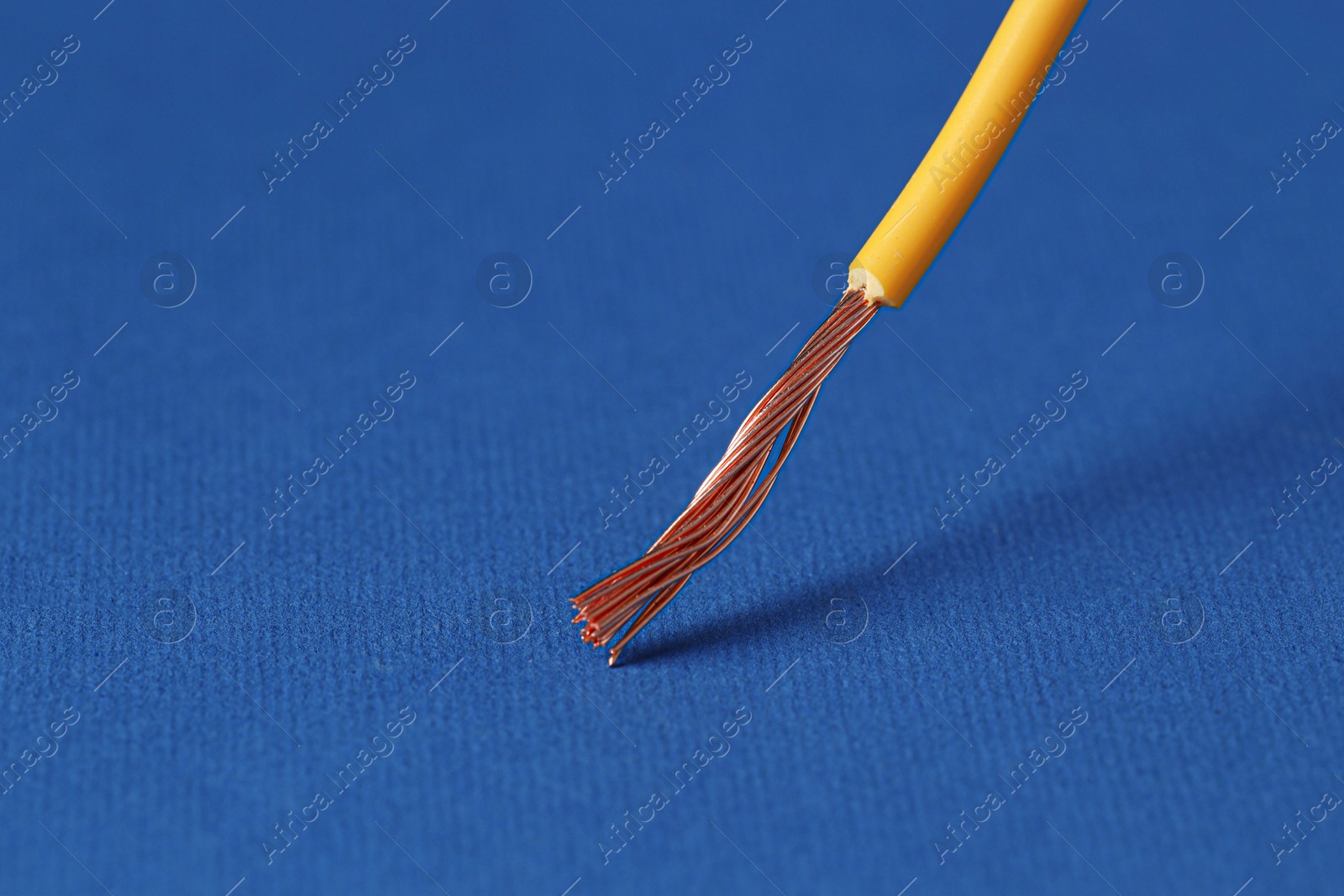 Photo of Yellow stripped electrical wire on blue background, closeup