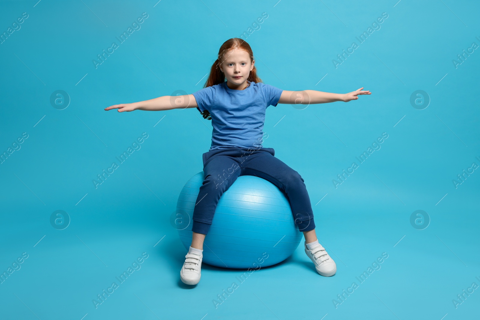 Photo of Cute little girl sitting on fitness ball against light blue background