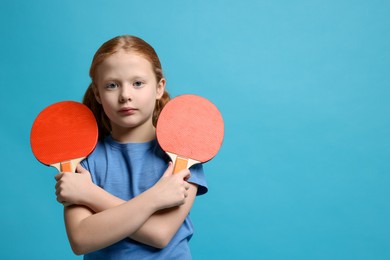 Photo of Little girl with ping pong rackets on light blue background, space for text