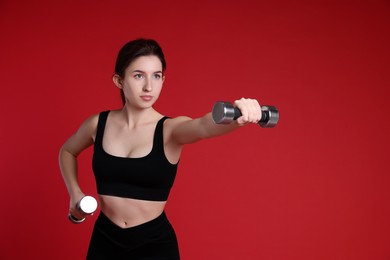 Woman in sportswear exercising with dumbbells on red background, space for text