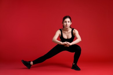 Woman in sportswear exercising on red background