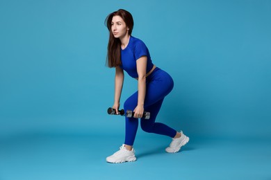 Photo of Woman in sportswear exercising with dumbbells on light blue background