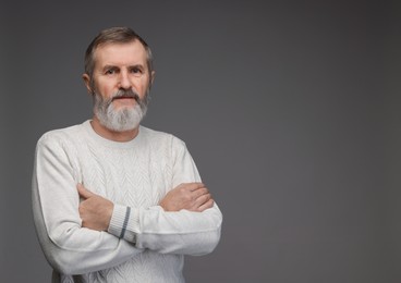 Portrait of mature man with crossed arms on grey background, space for text