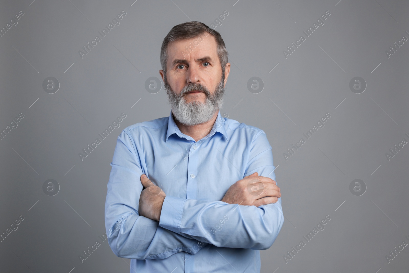 Photo of Portrait of mature man with crossed arms on grey background