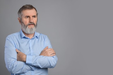 Portrait of mature man with crossed arms on grey background, space for text