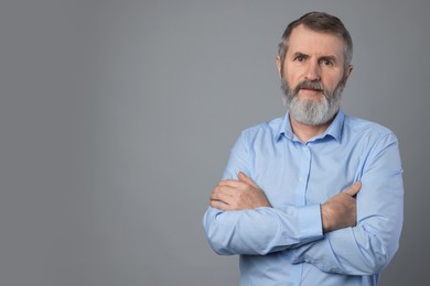 Portrait of mature man with crossed arms on grey background, space for text