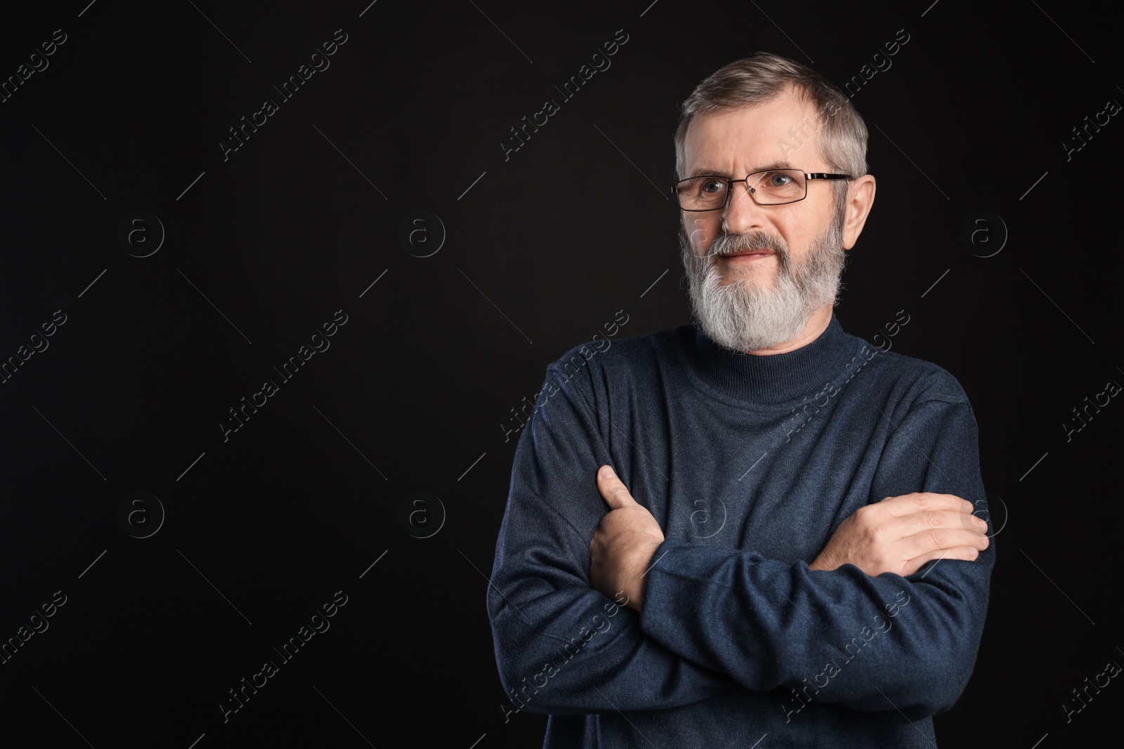 Photo of Portrait of mature man with crossed arms on black background, space for text