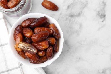 Photo of Tasty sweet dried dates in bowl and jar on white marble table, flat lay. Space for text