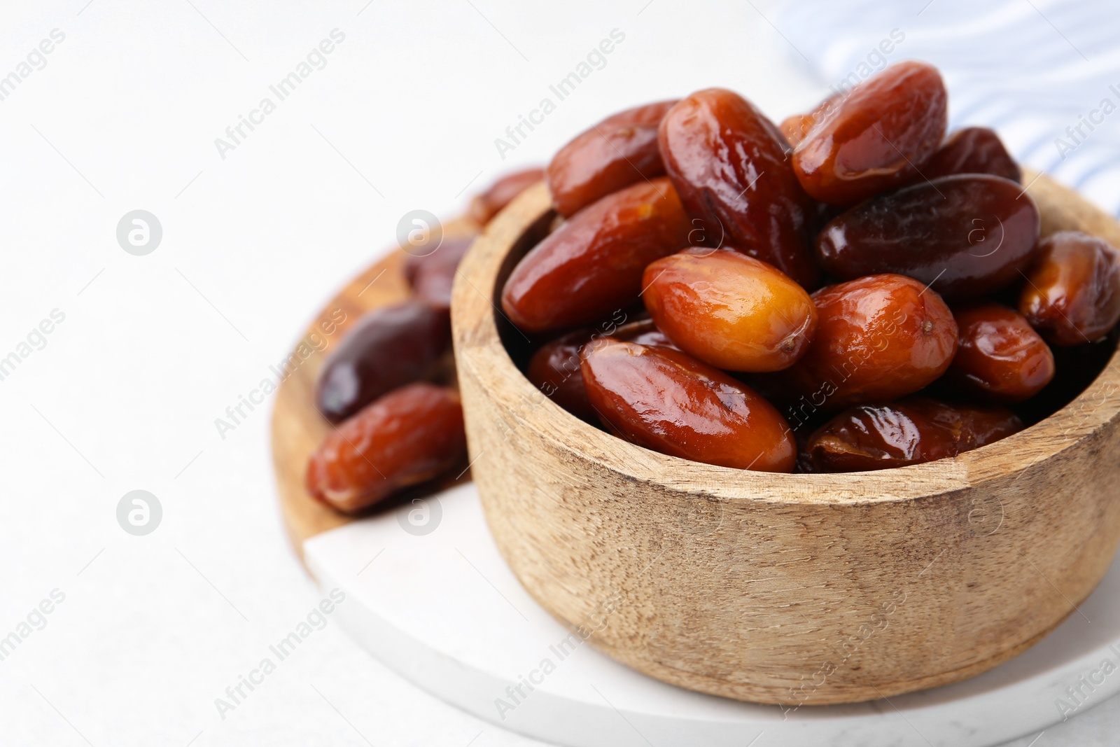 Photo of Tasty dried dates in wooden bowl on white table, closeup. Space for text