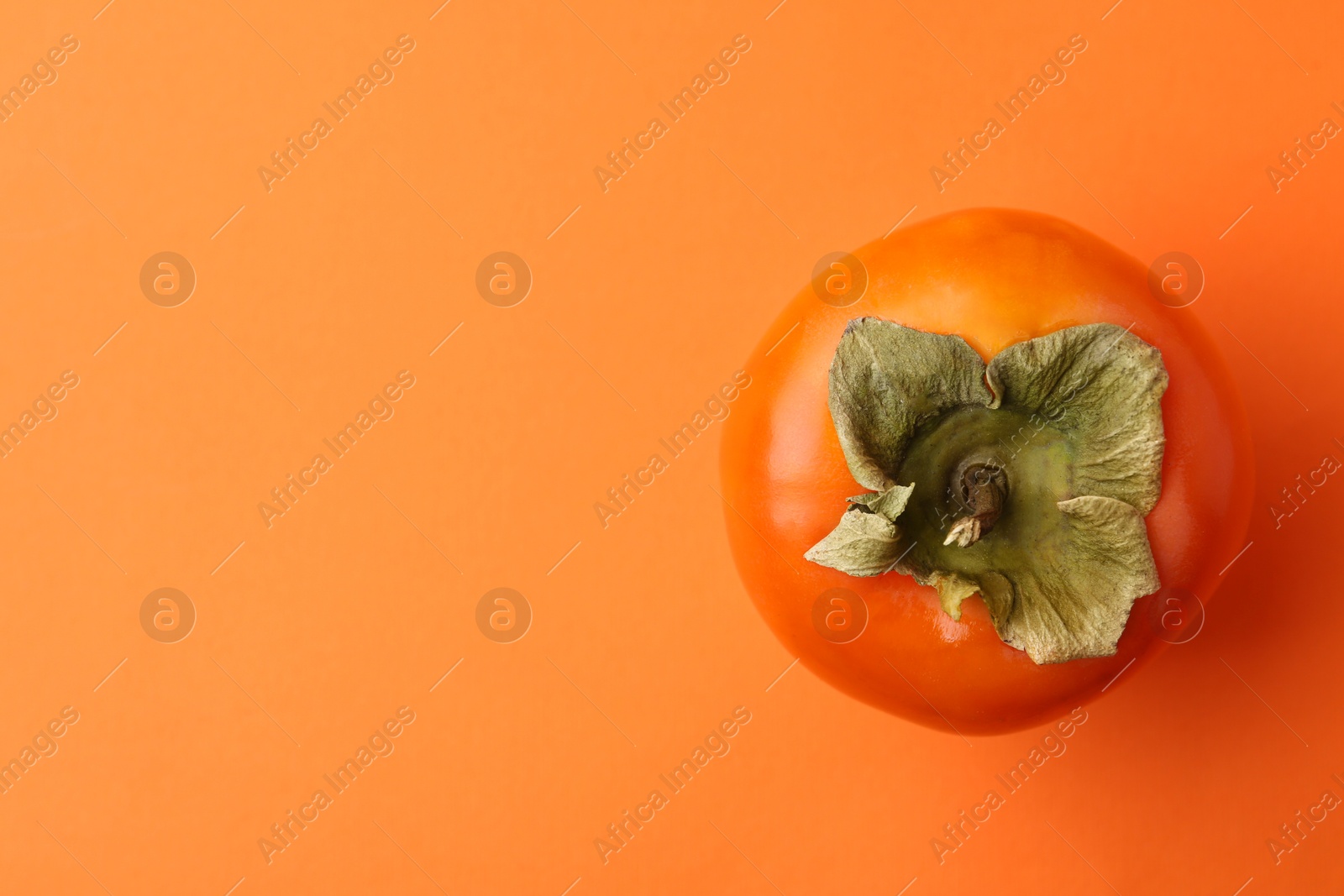 Photo of Delicious fresh juicy persimmon on orange table, top view. Space for text