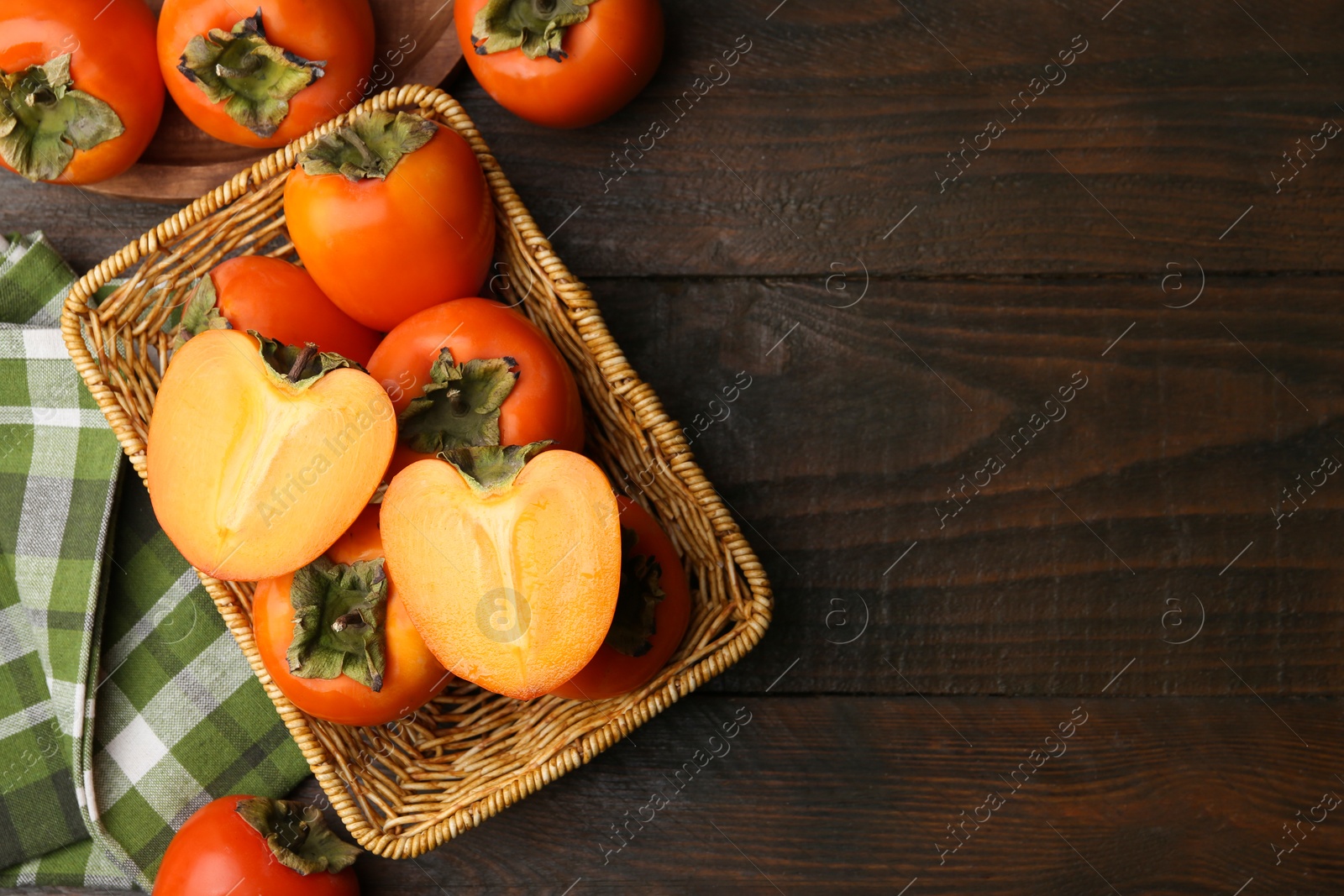 Photo of Delicious fresh juicy persimmons in wicker basket on wooden table, top view. Space for text