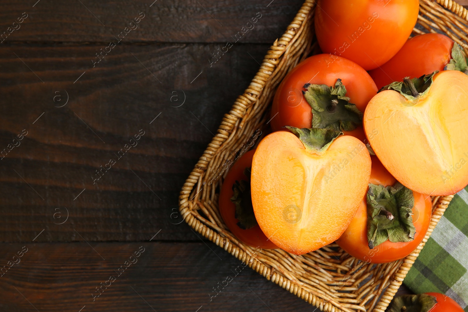 Photo of Delicious fresh juicy persimmons in wicker basket on wooden table, top view. Space for text