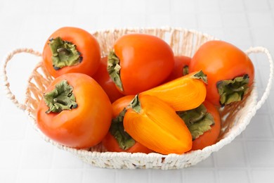 Photo of Ripe persimmons in wicker basket on white tiled table, closeup