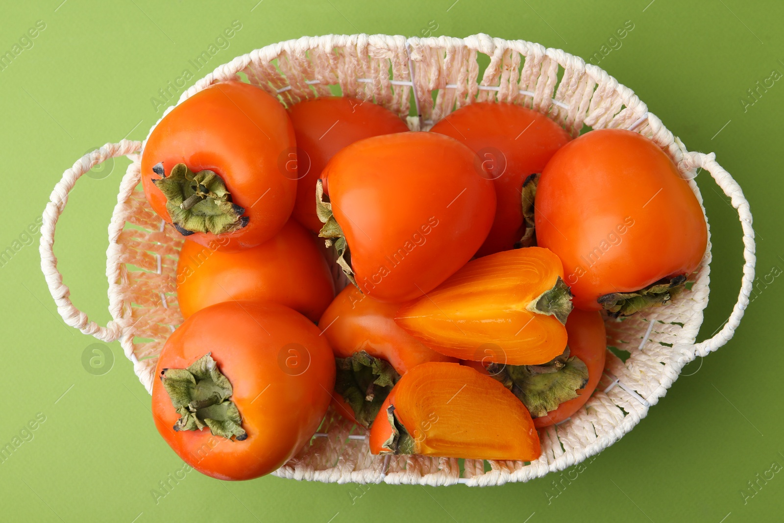 Photo of Ripe persimmons in wicker basket on green background, top view