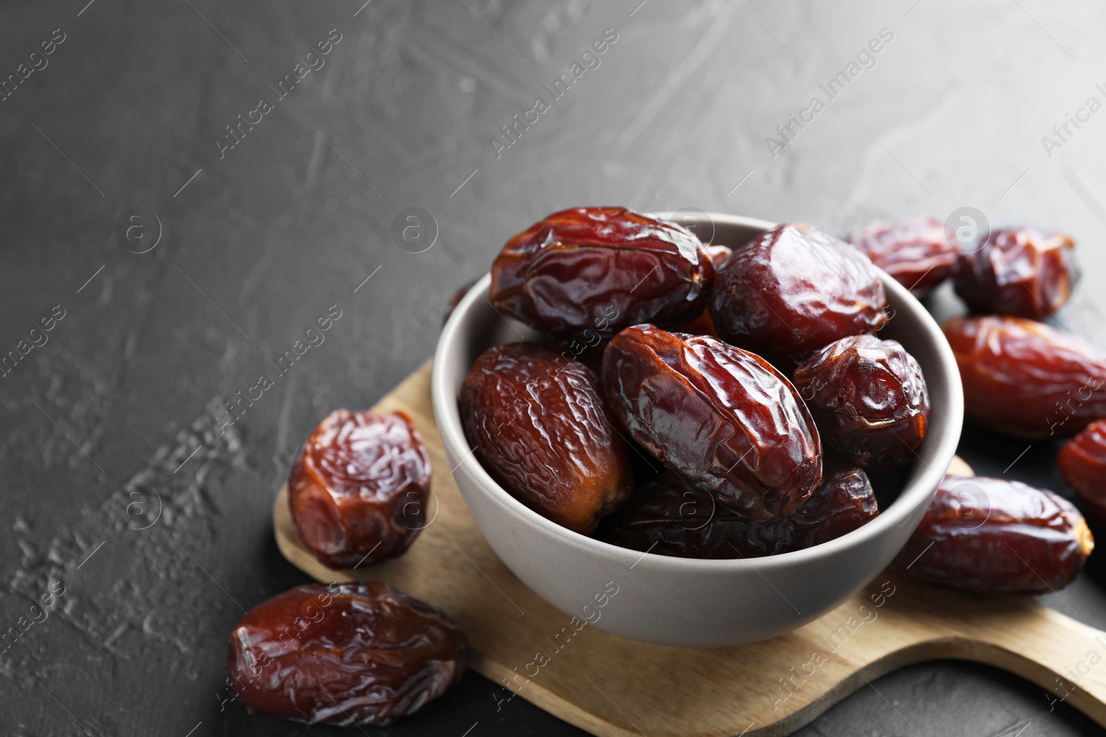 Photo of Tasty dried dates in bowl on grey table, closeup. Space for text