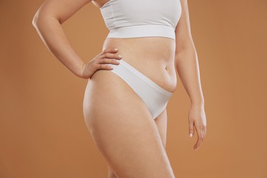 Woman with cellulite on light brown background, closeup